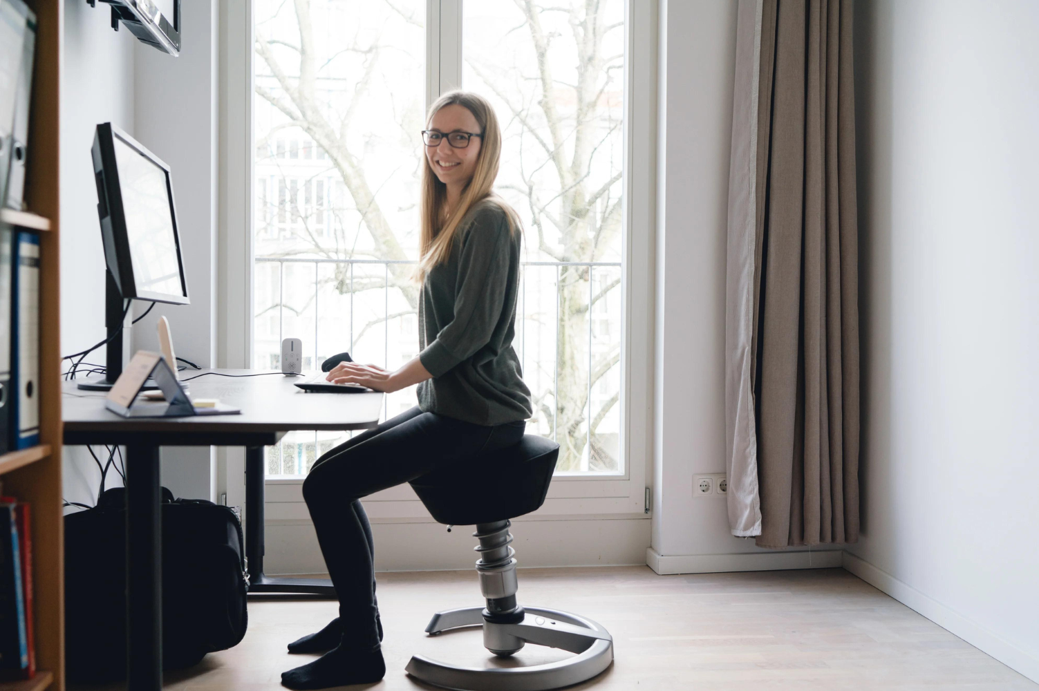 Eine Frau sitzt auf einem ergonomischen Stuhl vor einem Schreibtisch.