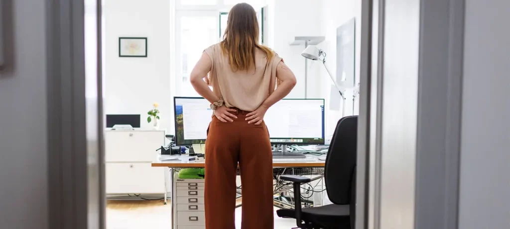 Eine Frau mit Rückenschmerzen steht in einem Büro.