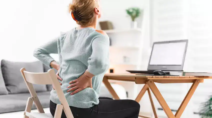 Frau mit Rückenschmerzen am Laptop – unergonomischer Arbeitsplatz im Homeoffice